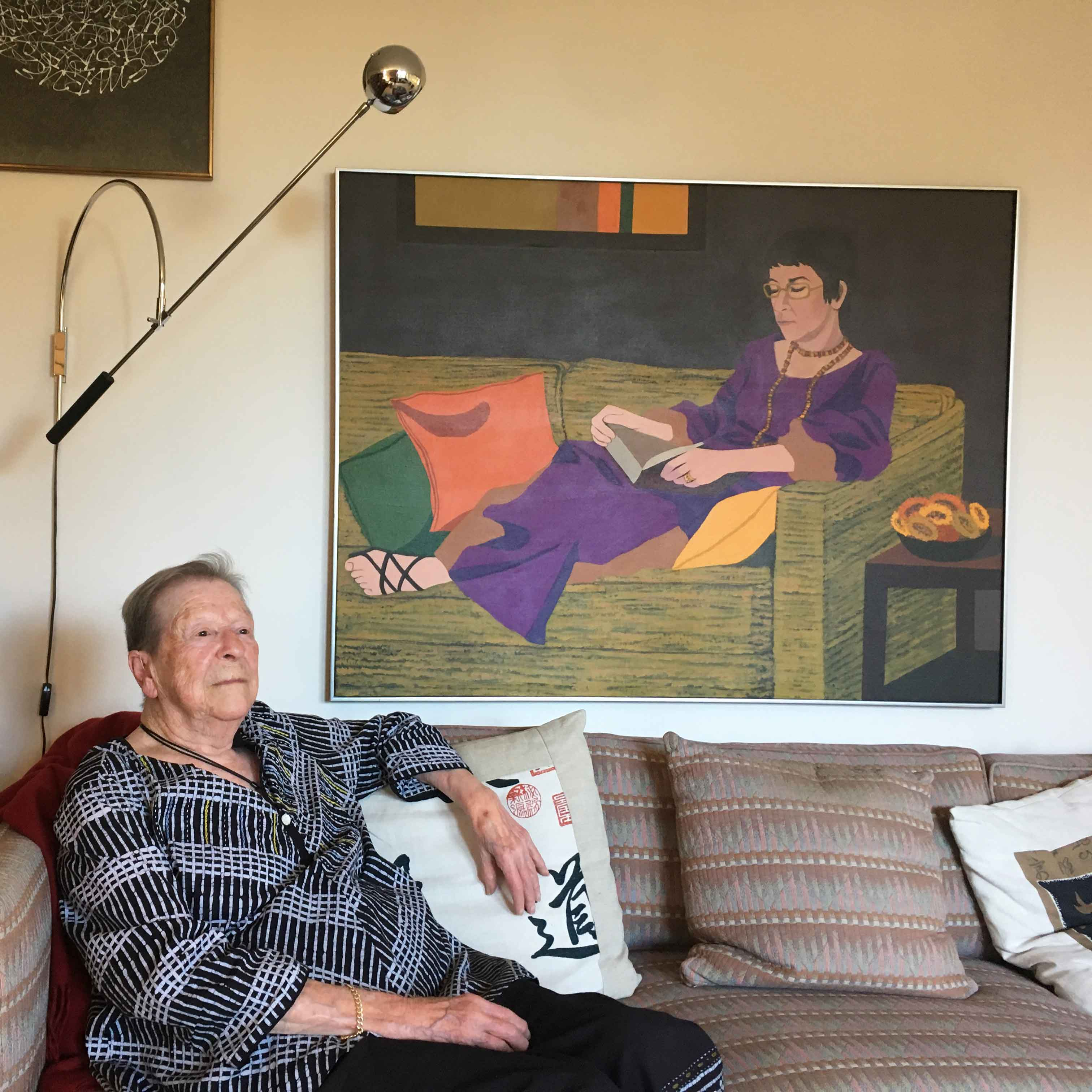 Professor Angela Little sits on a couch in front of a painting
