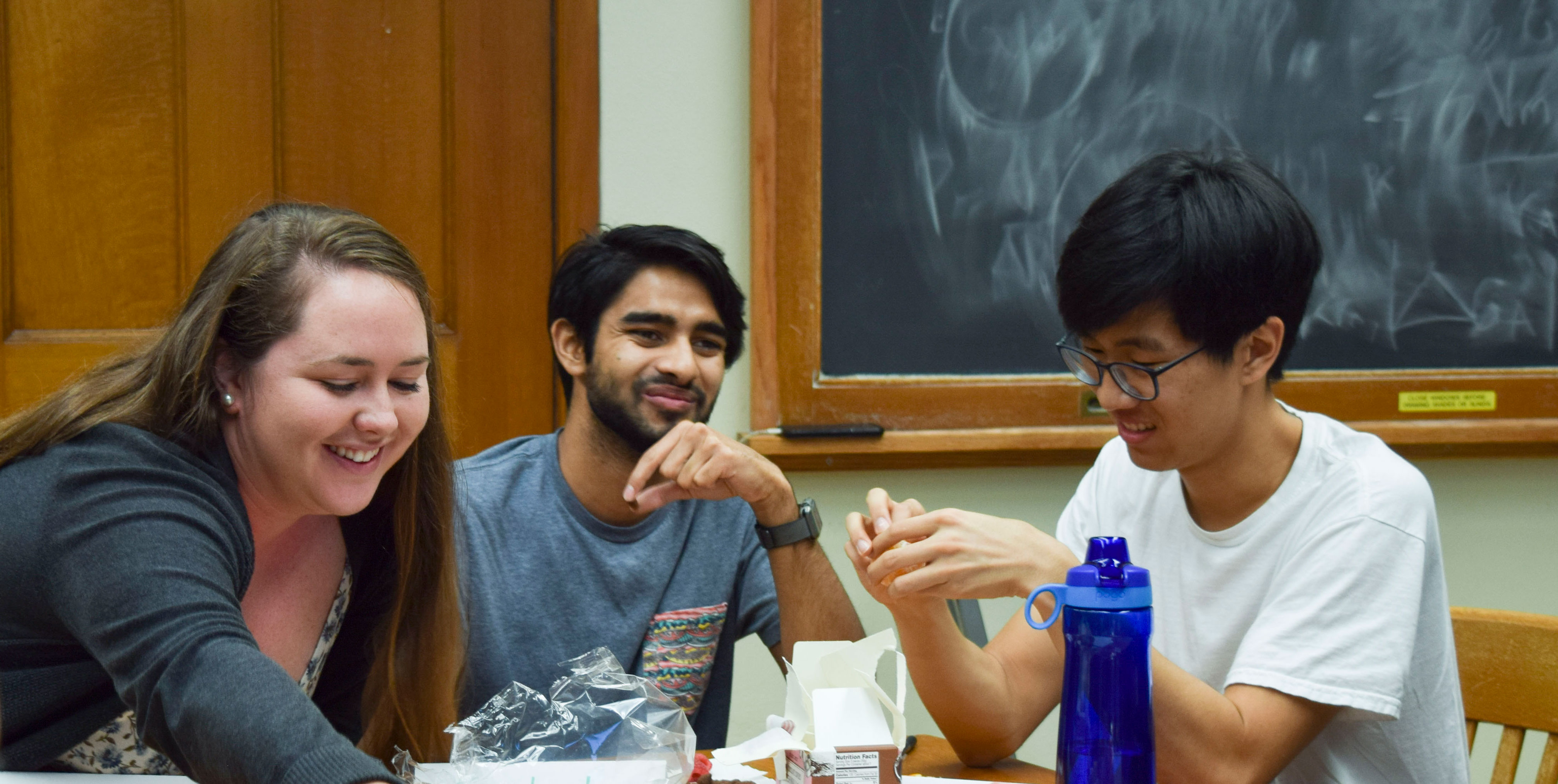 Three students sit at a table, listening to their instructor