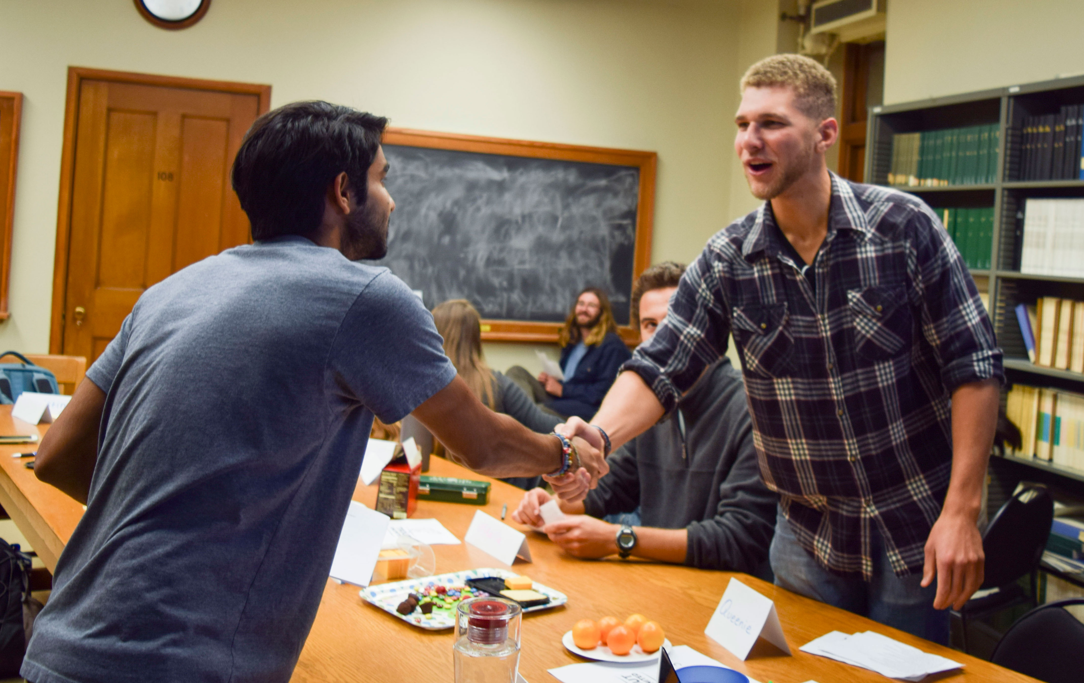 Two men stand to shake hands in a classroom