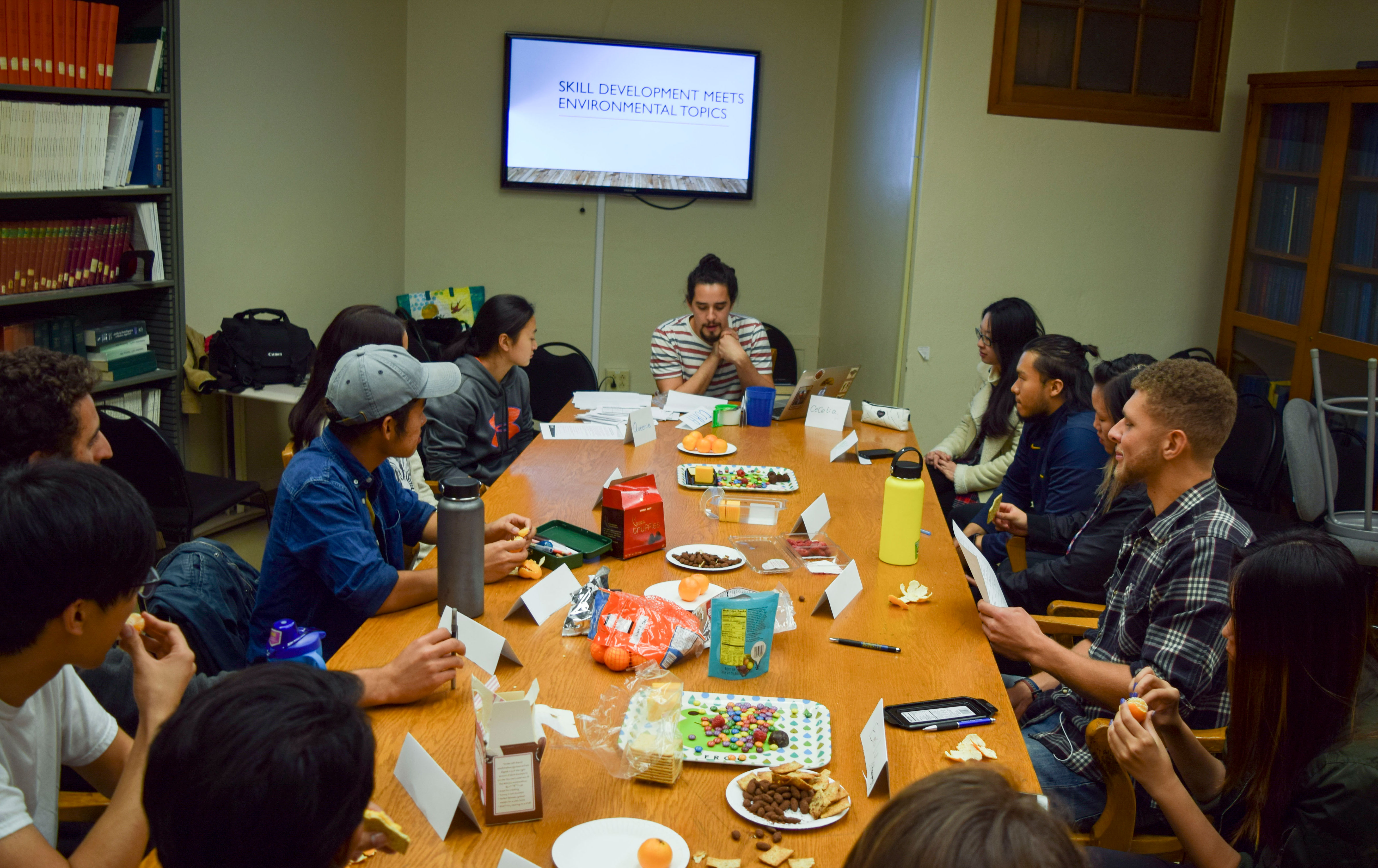 A teacher speaks to a group of students sitting around a large table