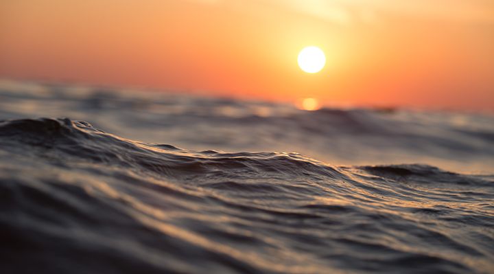 closeup on ocean water with a sun setting in the background