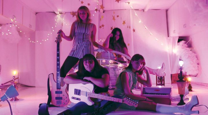 Four girls in a band posing in a pink room
