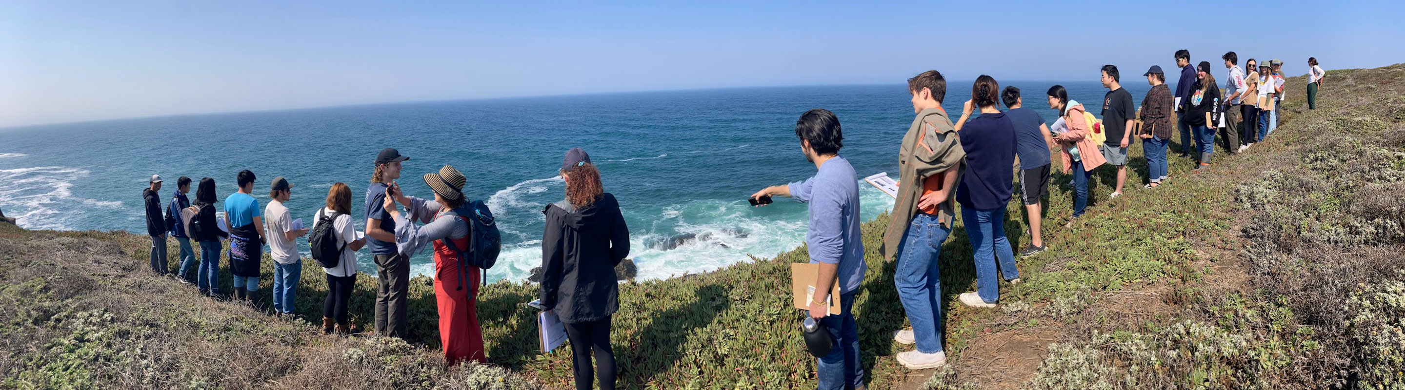 A group of people on a cliff looking down at the ocean
