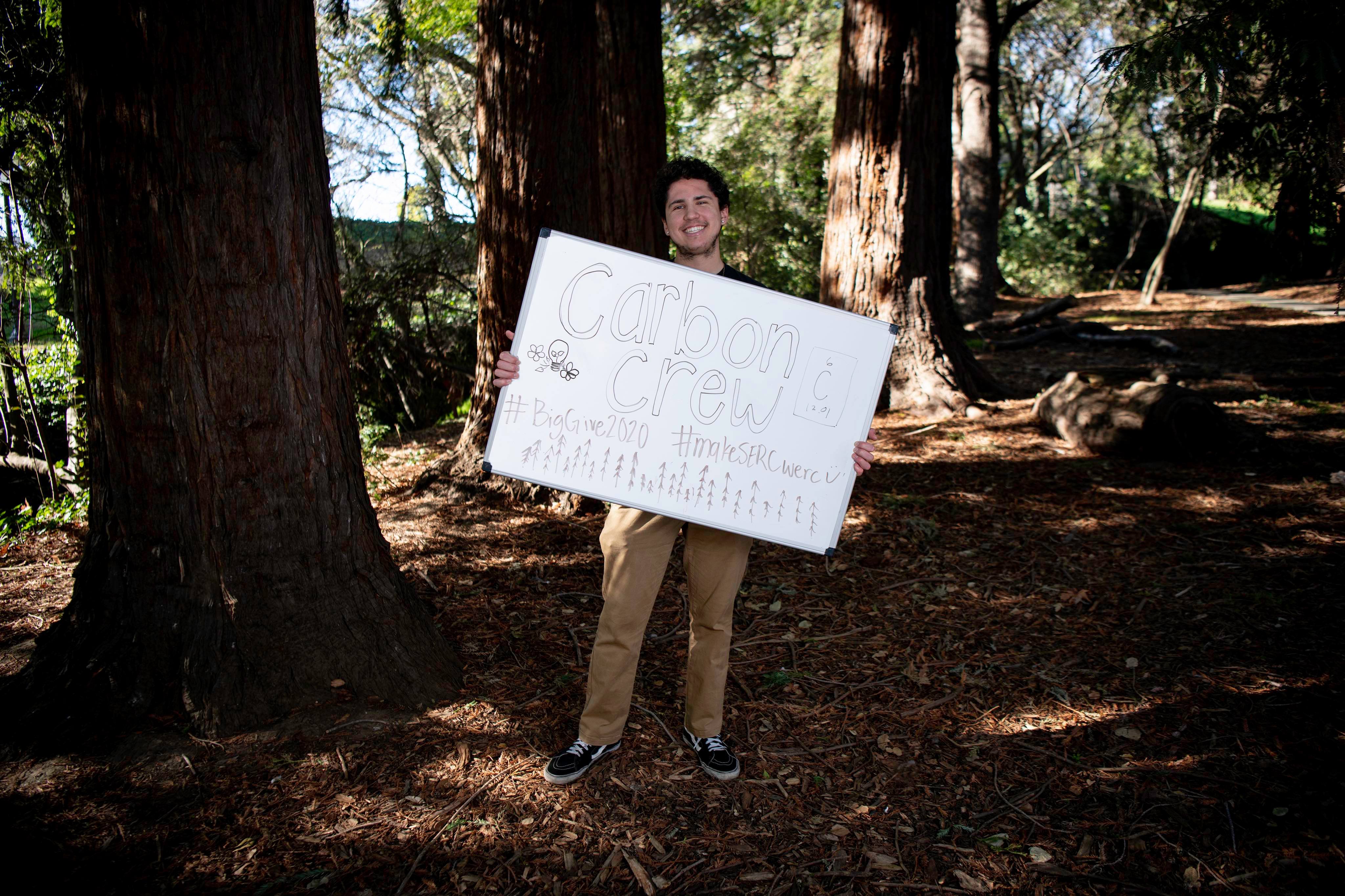 Dante holding a sign about SERC in front of a tree.