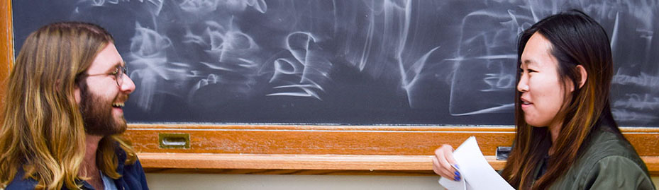 Two people sitting in front of a chalkboard