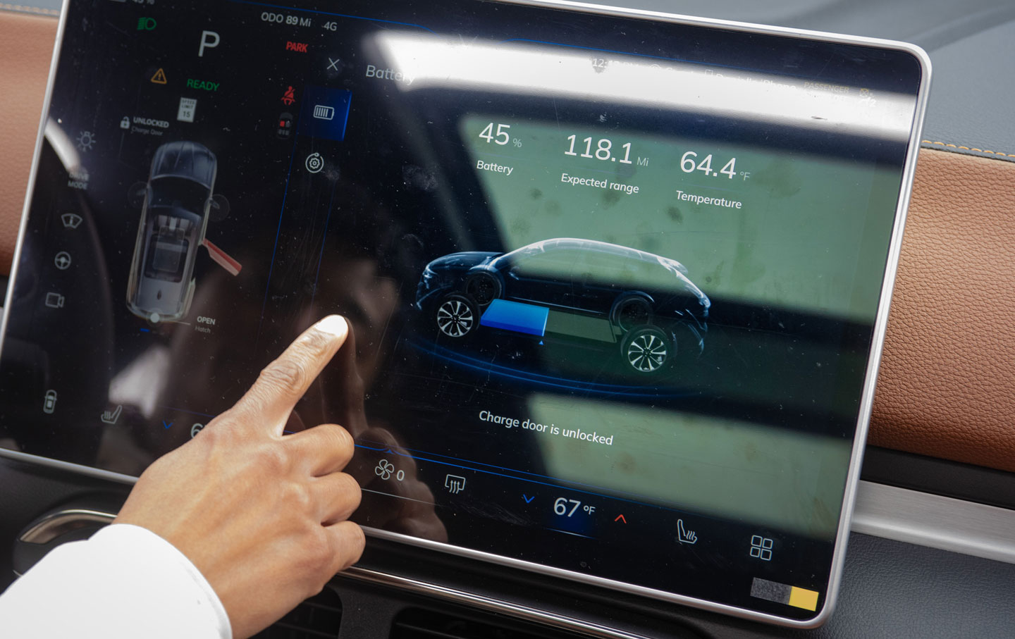 A finger points to a car screen displaying information about the vehicle's charging levels.