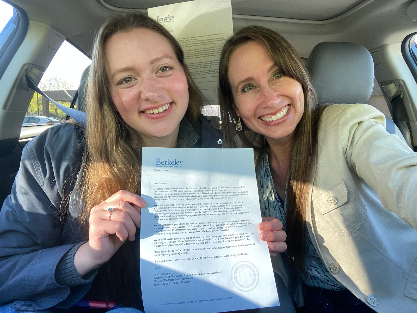 A photo of two women holding up a letter in a car.
