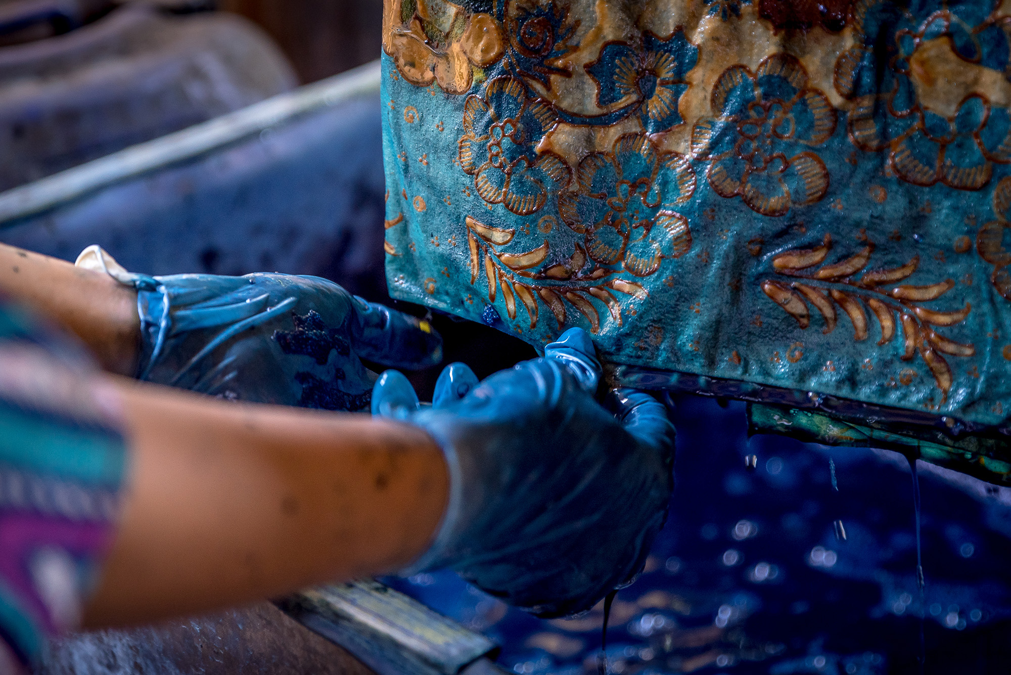 Hands in blue gloves holding fabric, both dripping in dye