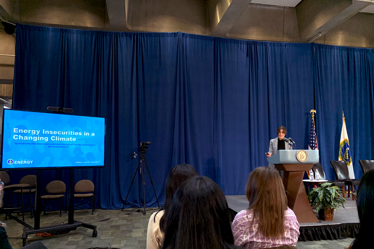 A photo of a woman standing in front of a lectern during a presentation.