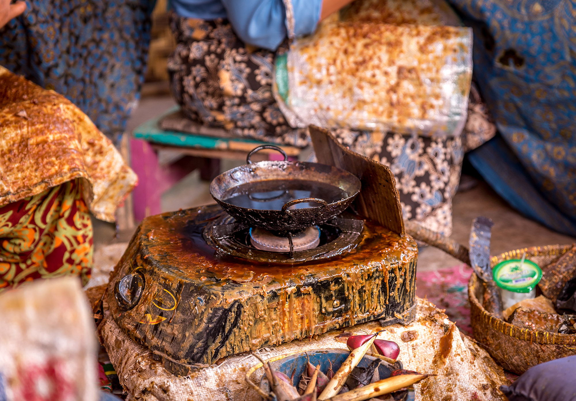 Metal bowl with dark liquid sits on a small gas burner which is covered in dry wax.