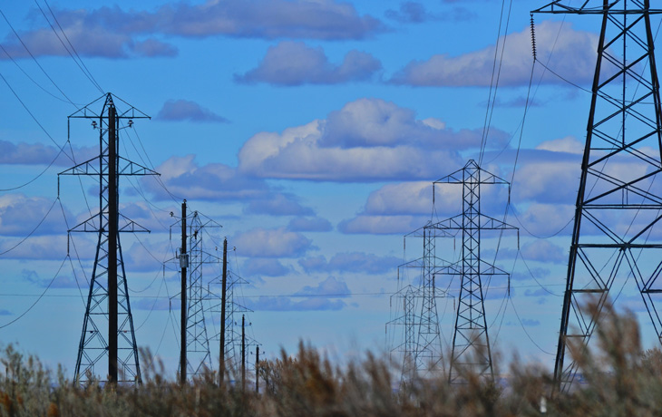 A photo of electric transmission lines against a blue sky with clouds.