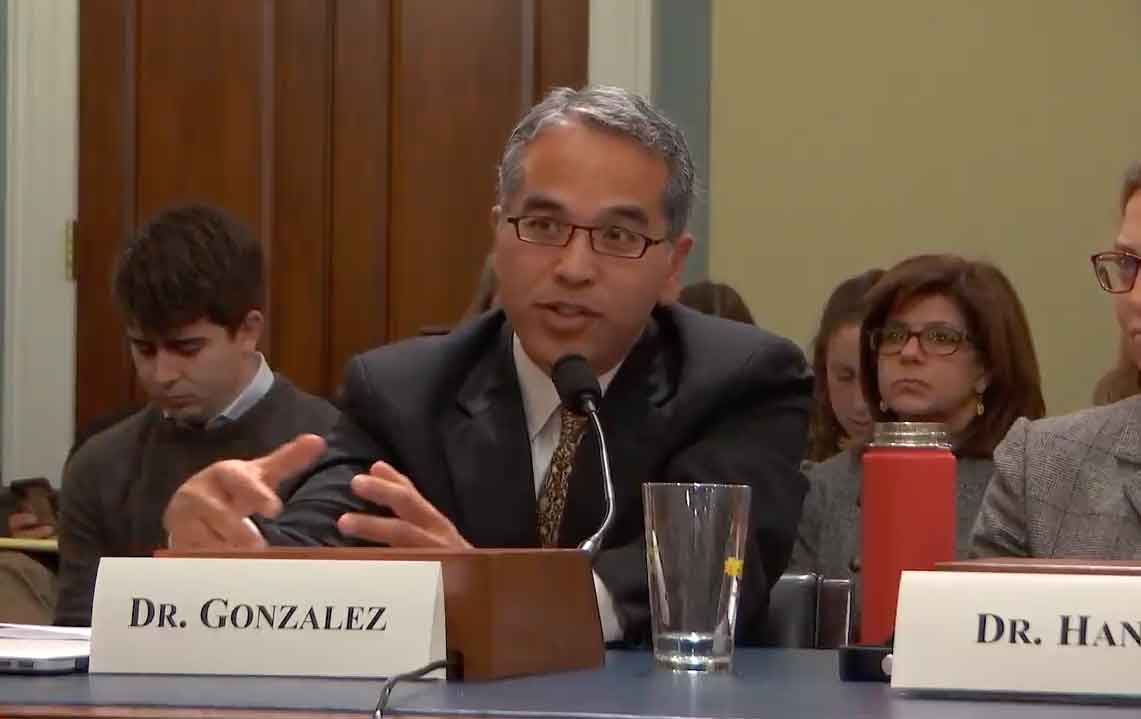 A man sits at a table in front of a microphone to testify in front of congress