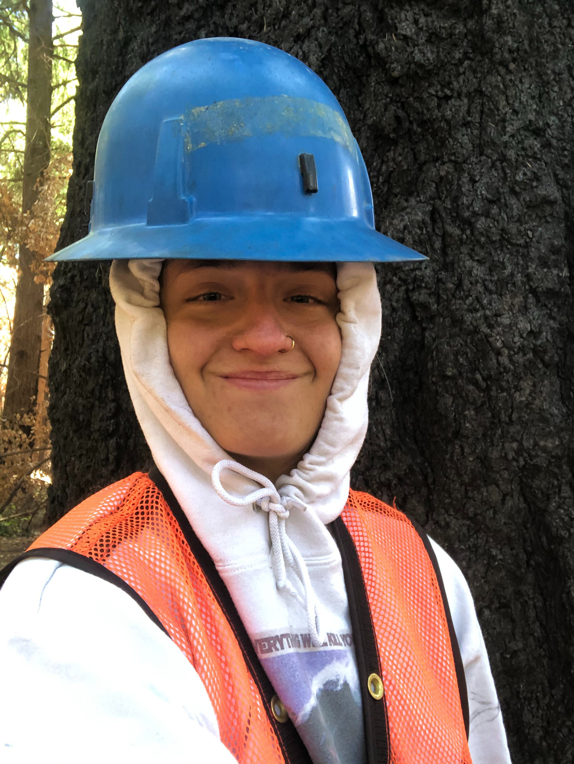 Hope Gale-Hendry wearing a blue hard hat and safety vest in front of a large tree.