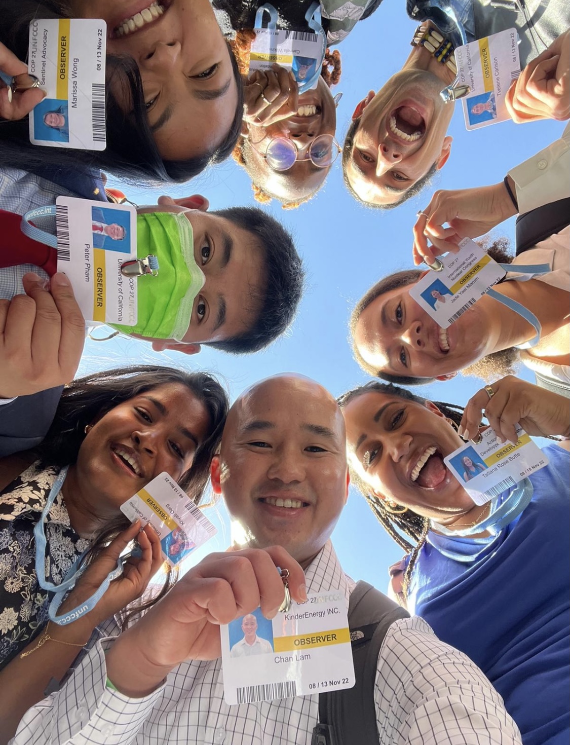 A group of people stare down at the camera holding badges near their faces.