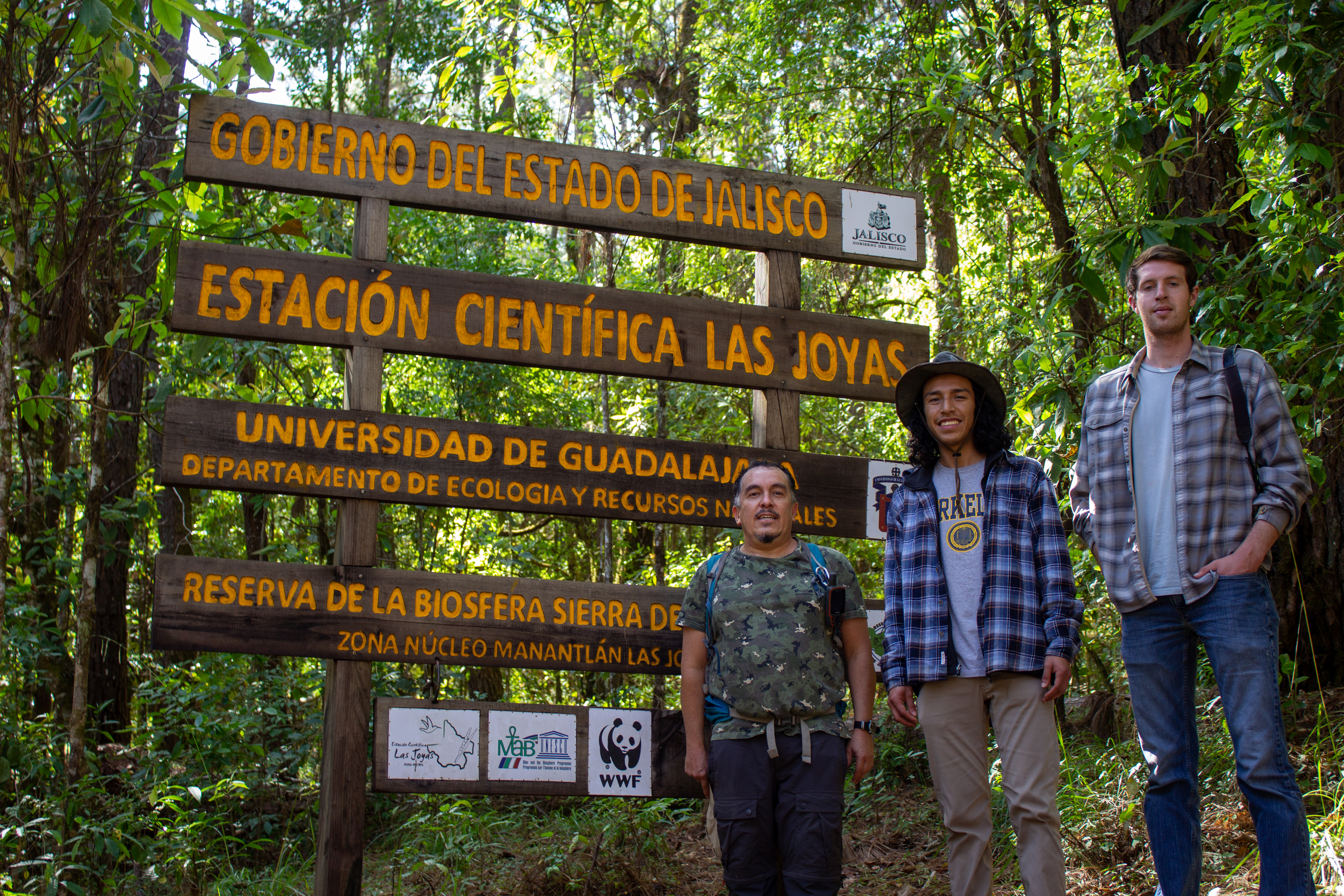 Aguilar standing with two others next to a sign in a forest that reads "Gobierno Del Estado de Jalisco"