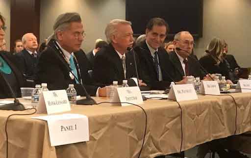 Four men sit at a table in front of microphones to testify before congress