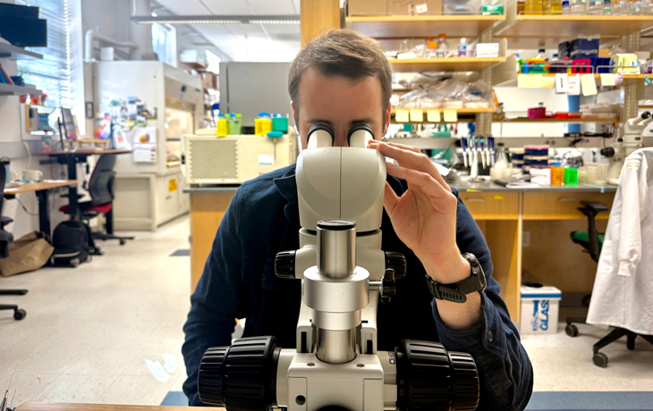 A photo of a man at a microscope in a lab environment.