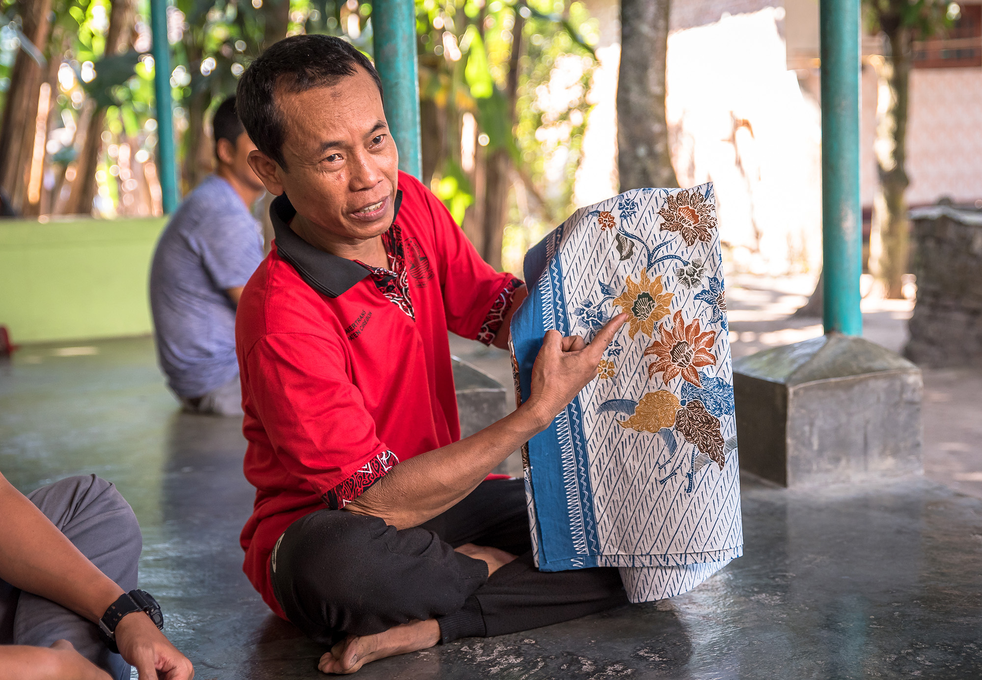 Man sitting, holding blue batik.