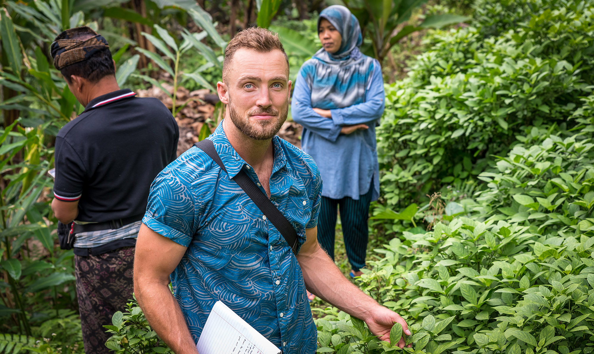 Matt Mayes standing in a field, with one man and one woman behind him.