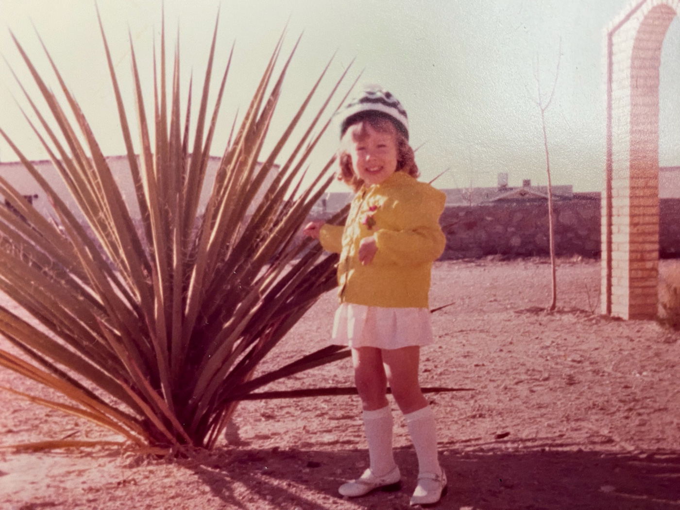 A vintage photo of a young girl standing next to a large spiny plant.