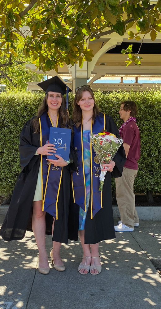 A photo of two women in graduation regalia holding up a program.