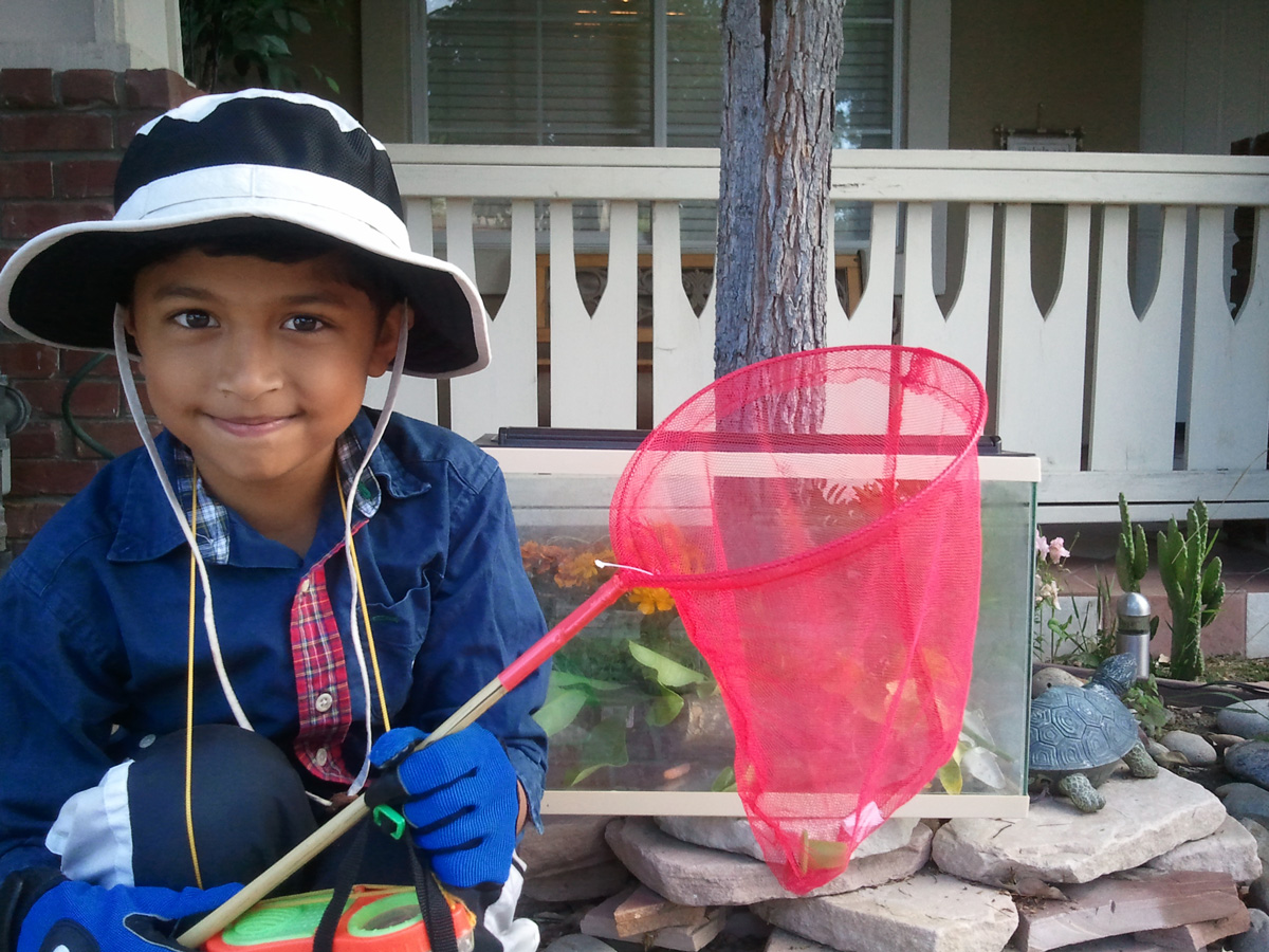 A young child looks at the camera while holding a net and wearing a hat.
