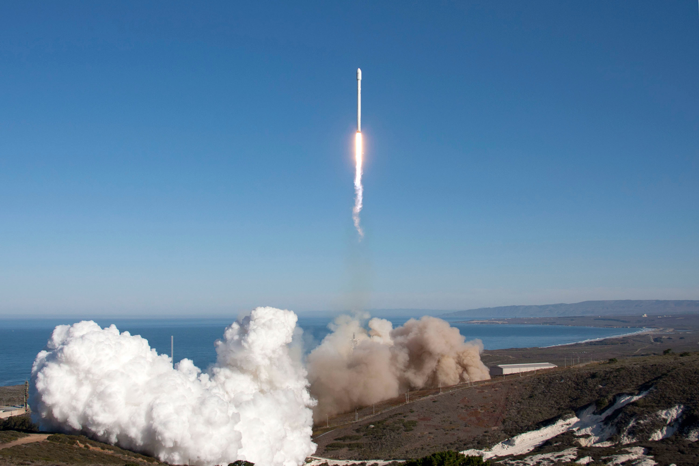 A space rocket launches from a coastal launch pad.