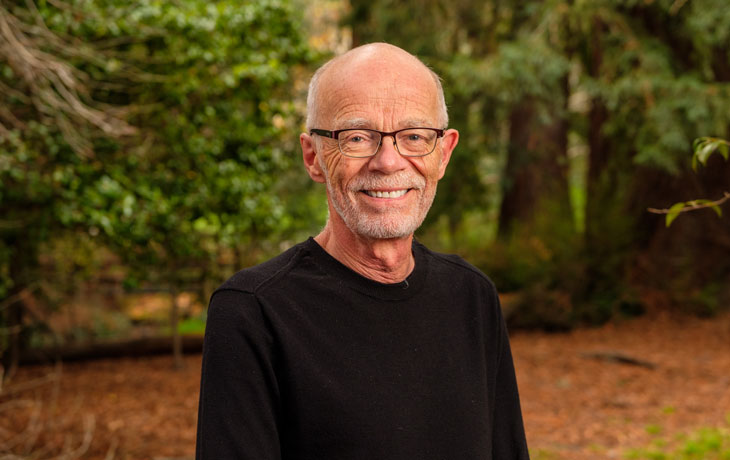 Headshot portrait of PMB professor John Taylor with forest/woodland backdrop