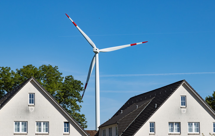 A photo of a wind turbine in between the roofs of two homes.