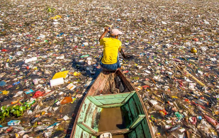 Adobe stock image of man on boat, surrounded by a pool of plastic and waste. 