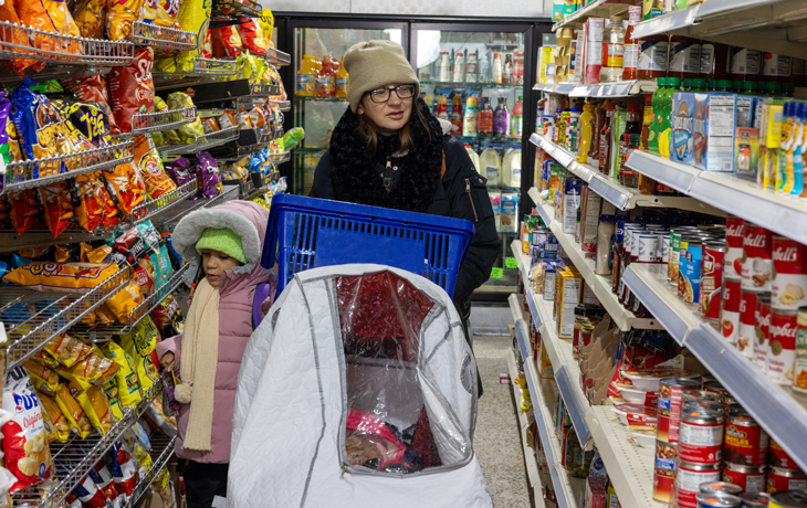A woman and child walk through the aisles of a grocery store. Several food packages are visible on both sides of them.