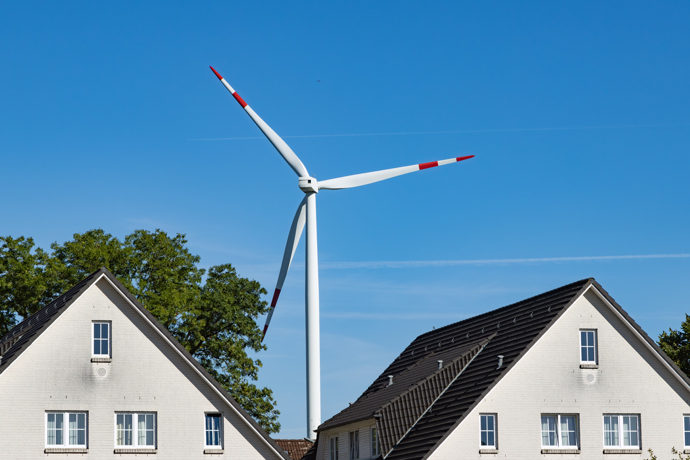 A photo of a wind turbine in between the roofs of two homes.