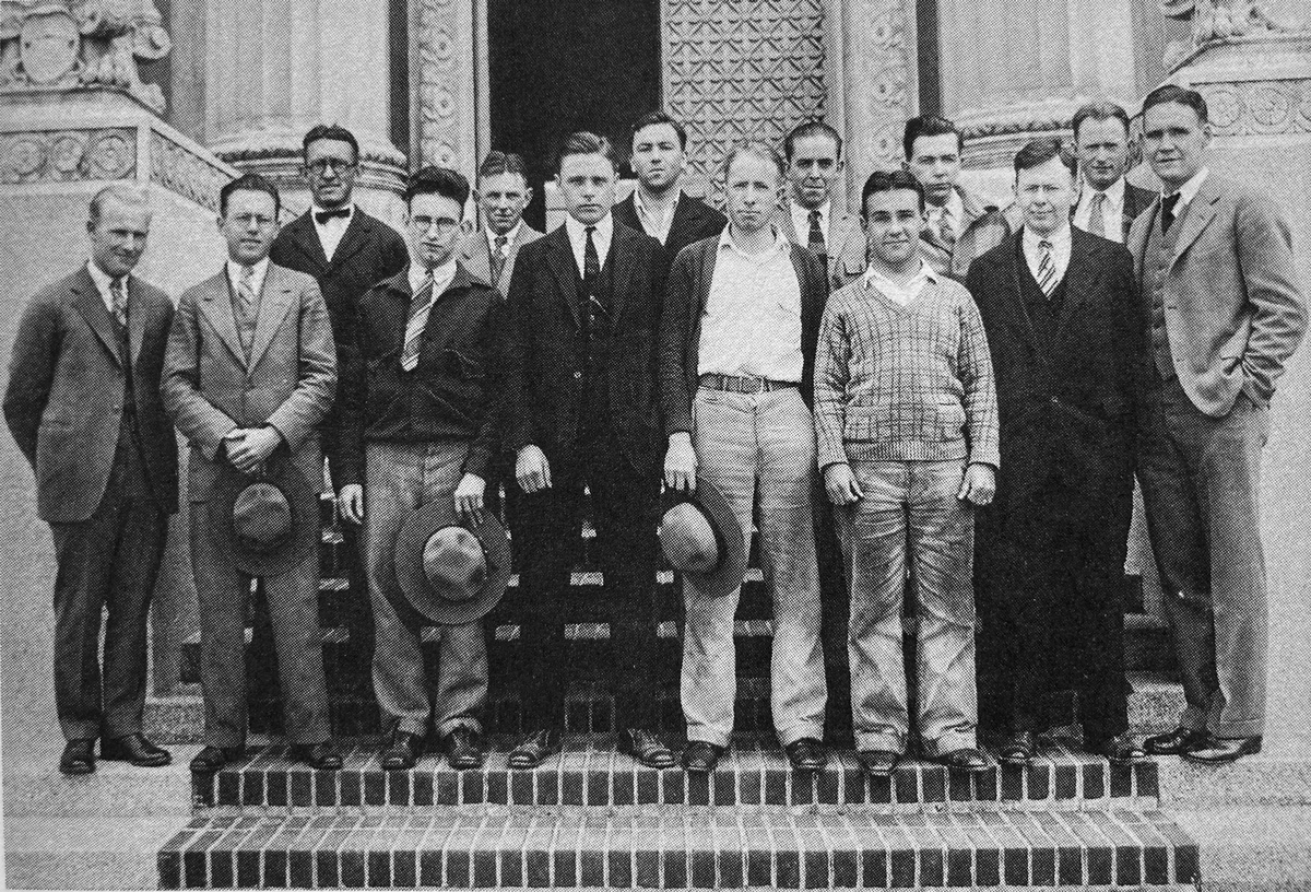 A black and white photo of men standing in front of a building.