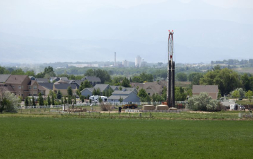 Image of a neighborhood near a tall Hydraulic-fracturing equipment towering over the homes but placed closely to the neighborhood.