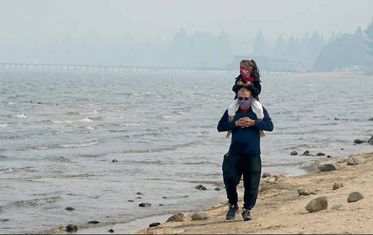 A person with their child on their shoulders on the beach.