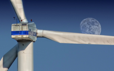 Close up of a wind turbine against the sky with a visible moon