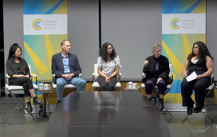 A group of people sit in chairs and talk on a panel.