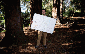 Dante holding a sign about SERC in front of a tree.