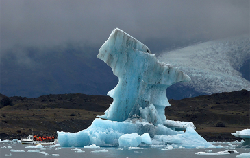 A large iceberg with a small boat of people in life vests next to it.