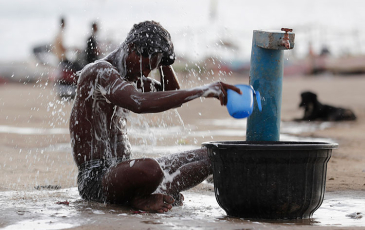 An Indian man pouring water on himself at a public fountain.
