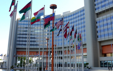 An photo showing the exterior of the United Nations building in Vienna, with multiple flags representing several member nations visible.