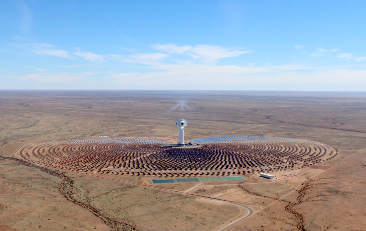 A bird's eye view of solar power plant with several panels and a large tower in a desert environment.