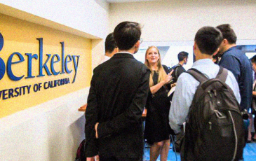 A woman speaking to two students next to a Berkeley sign.