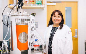 A portrait of PMB professor Cecilia Martinez-Gomez next to a bioreactor in her lab.