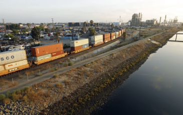 A railroad with cargo on it shown beside a large waterway.