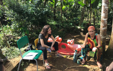 Two people sitting on chairs in a rainforest, talking.