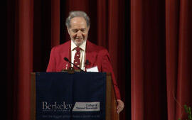 Jared Diamond standing at a podium, wearing a red jacket