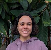 Headshot of Anela Napoleon with green plants in the background